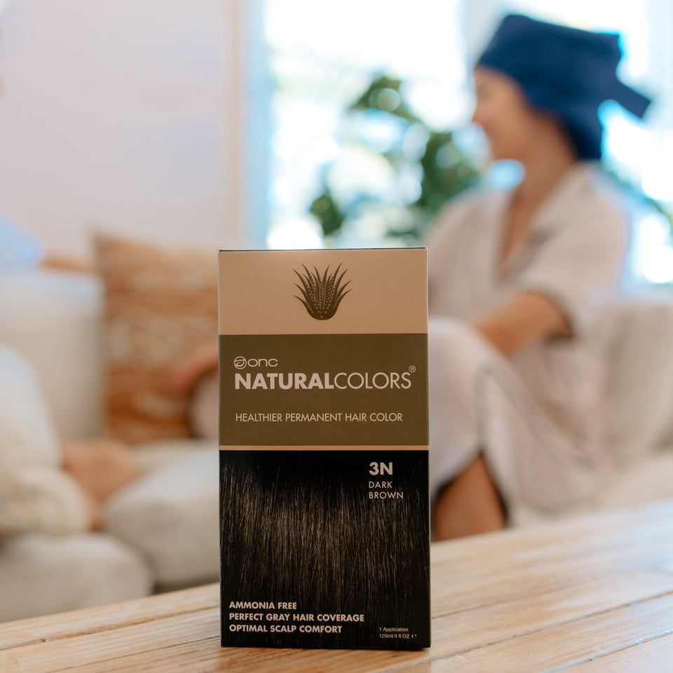 A box of ONC NATURALCOLORS 3N Natural Dark Brown Heat Activated Hair Dye with Organic Ingredients 120 mL / 4 fl. oz. on a coffee table in front of two women chatting while wearing ONC NATURALCOLORS Heat Cap for ONC Heat Activated Hair Color